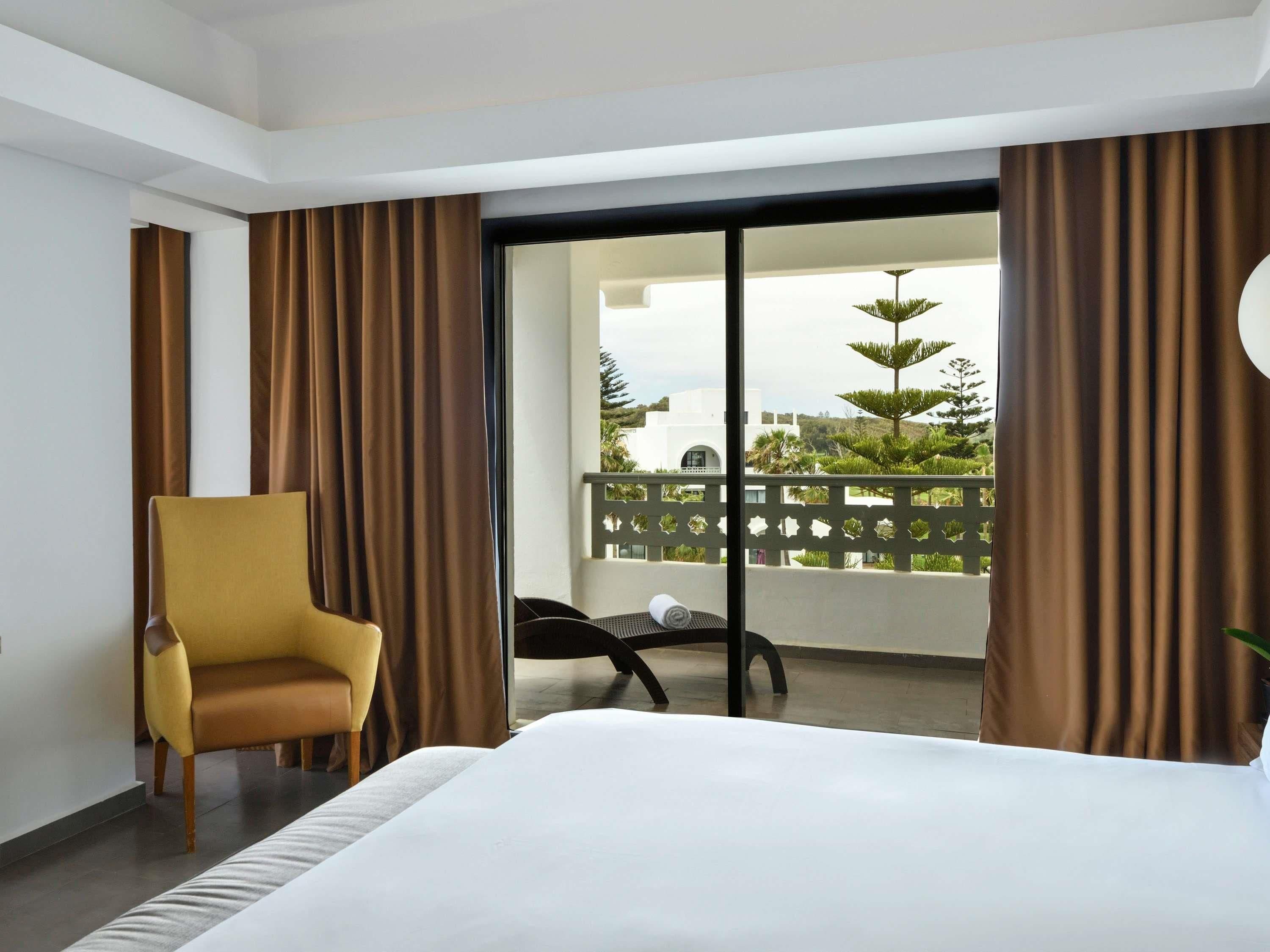 A hotel room with a bed, a chair, and a balcony with a view.