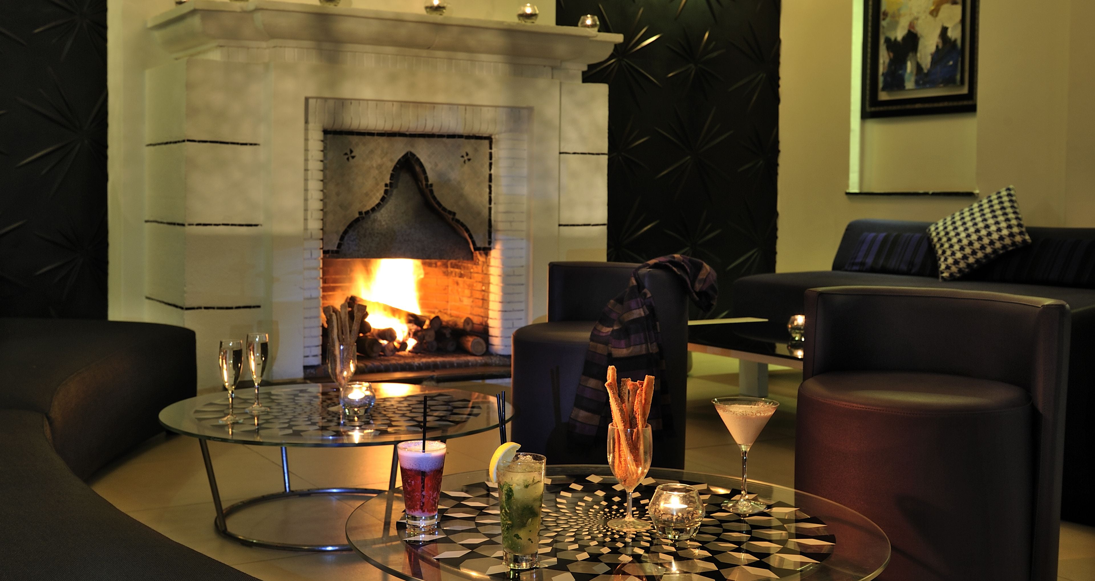 A cozy lounge area with a fireplace, leather seating, and a glass table with drinks and snacks.