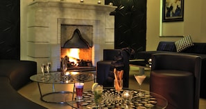 Un área de descanso acogedora con chimenea, asientos de cuero y una mesa de vidrio con bebidas y aperitivos.