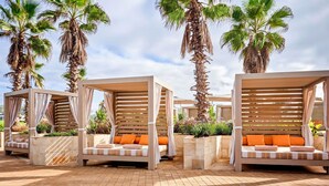 Eine Reihe von Außenlounges mit Holz-Pergolen, gepolsterten Sitzgelegenheiten und Palmen.