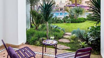 Un patio con dos sillas moradas, una mesa pequeña con una bandeja de comida y vistas a una piscina y follaje.