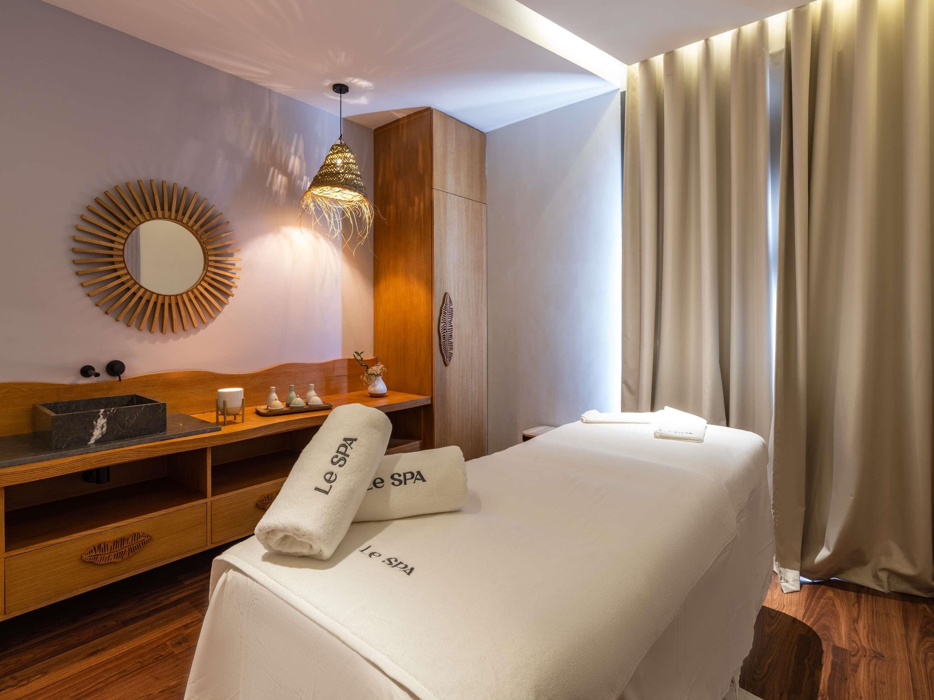 Une salle de spa avec un meuble-lavabo en bois, un miroir, un luminaire suspendu et un lit agrémenté de serviettes étiquetées « Le SPA ».