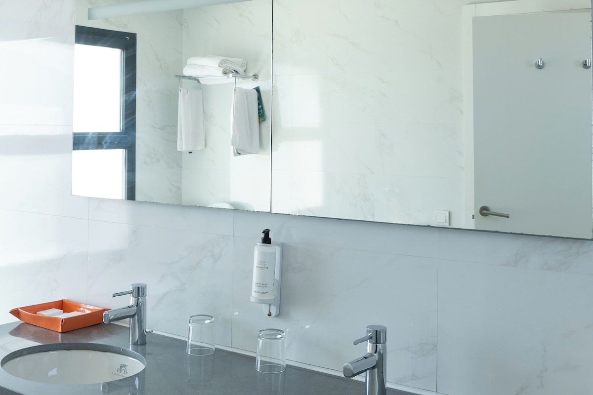 Un baño moderno con dos lavamanos, un espejo grande y una cabina de ducha de vidrio.