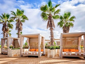 Une série d’espaces de détente en plein air, dotés de pergolas en bois, de sièges confortables et de palmiers.