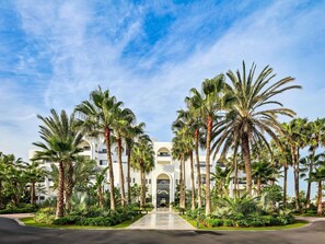 A hotel entrance with a central archway, surrounded by palm trees and greenery. - Pullman Mazagan Royal Golf & Spa El Jadida (El Jadida)
