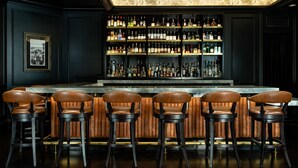 Un espace bar doté d’un comptoir en marbre, de tabourets de bar en cuir et d’un mur où sont exposées des bouteilles d’alcool.