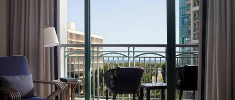 A hotel room with a balcony, a sofa, a chair, a small table, and a lamp.