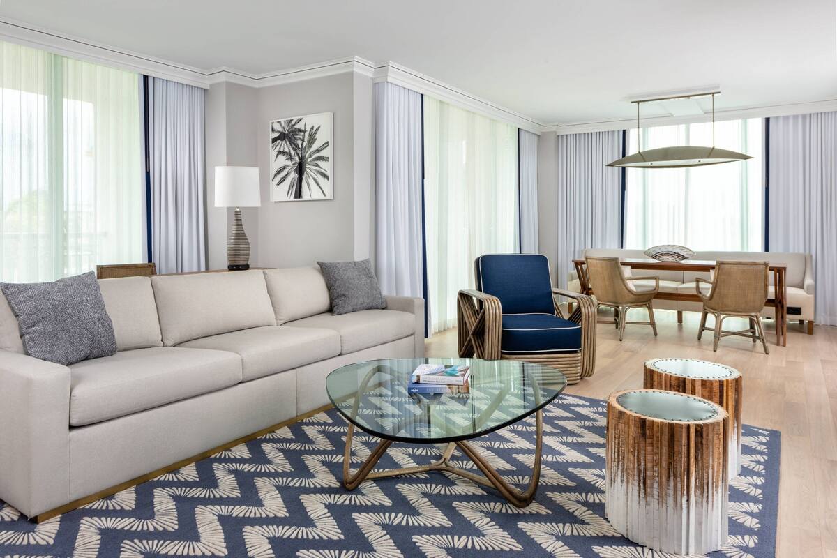 A modern living room with a sofa, a glass coffee table, and a dining area with chairs and a table.