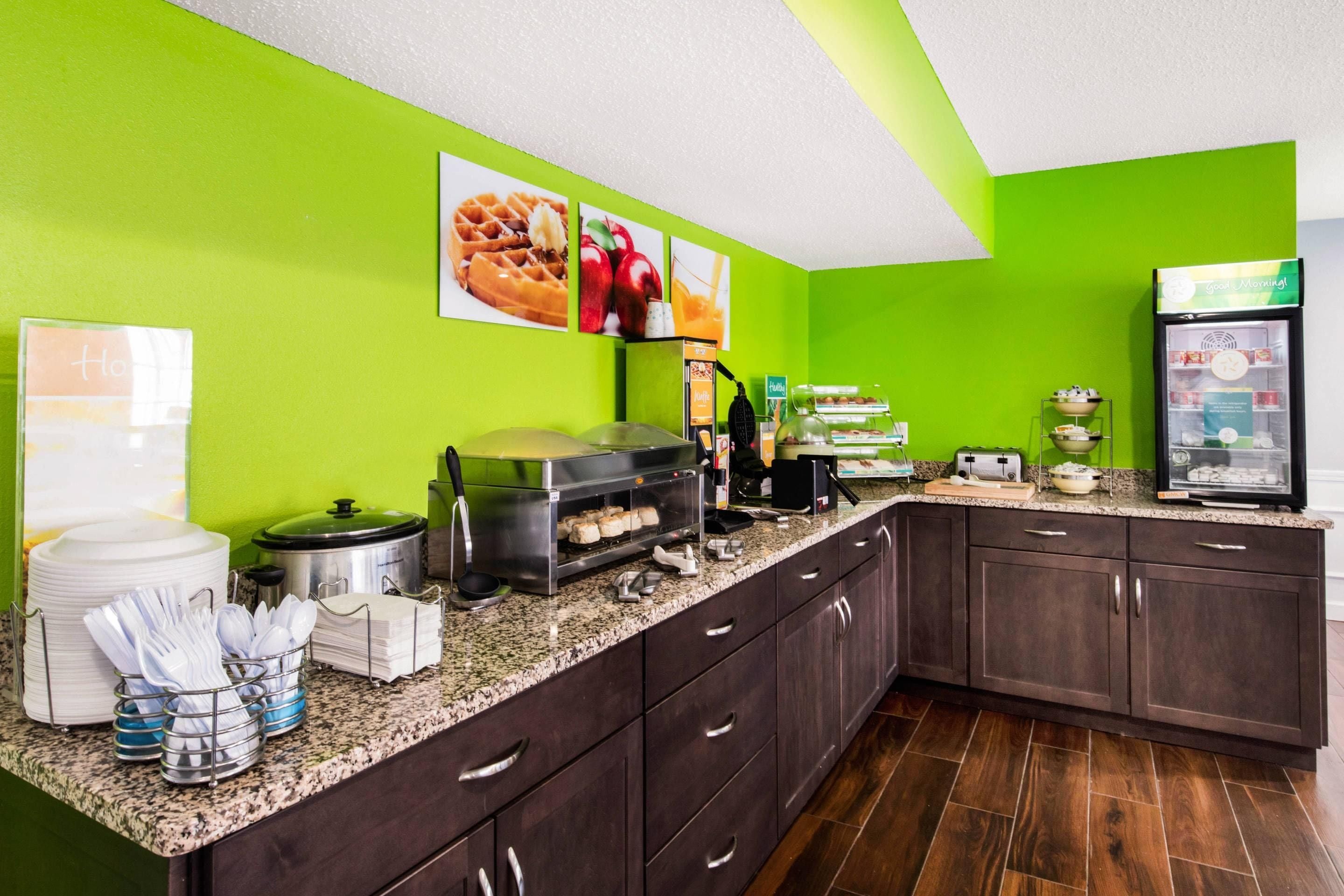 A kitchen with a green wall, a buffet counter with food items, and a refrigerator.