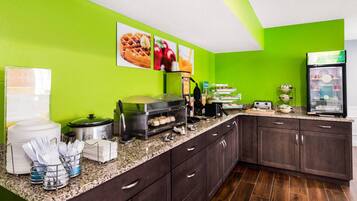 A kitchen with a green wall, a buffet counter with food items, and a refrigerator.