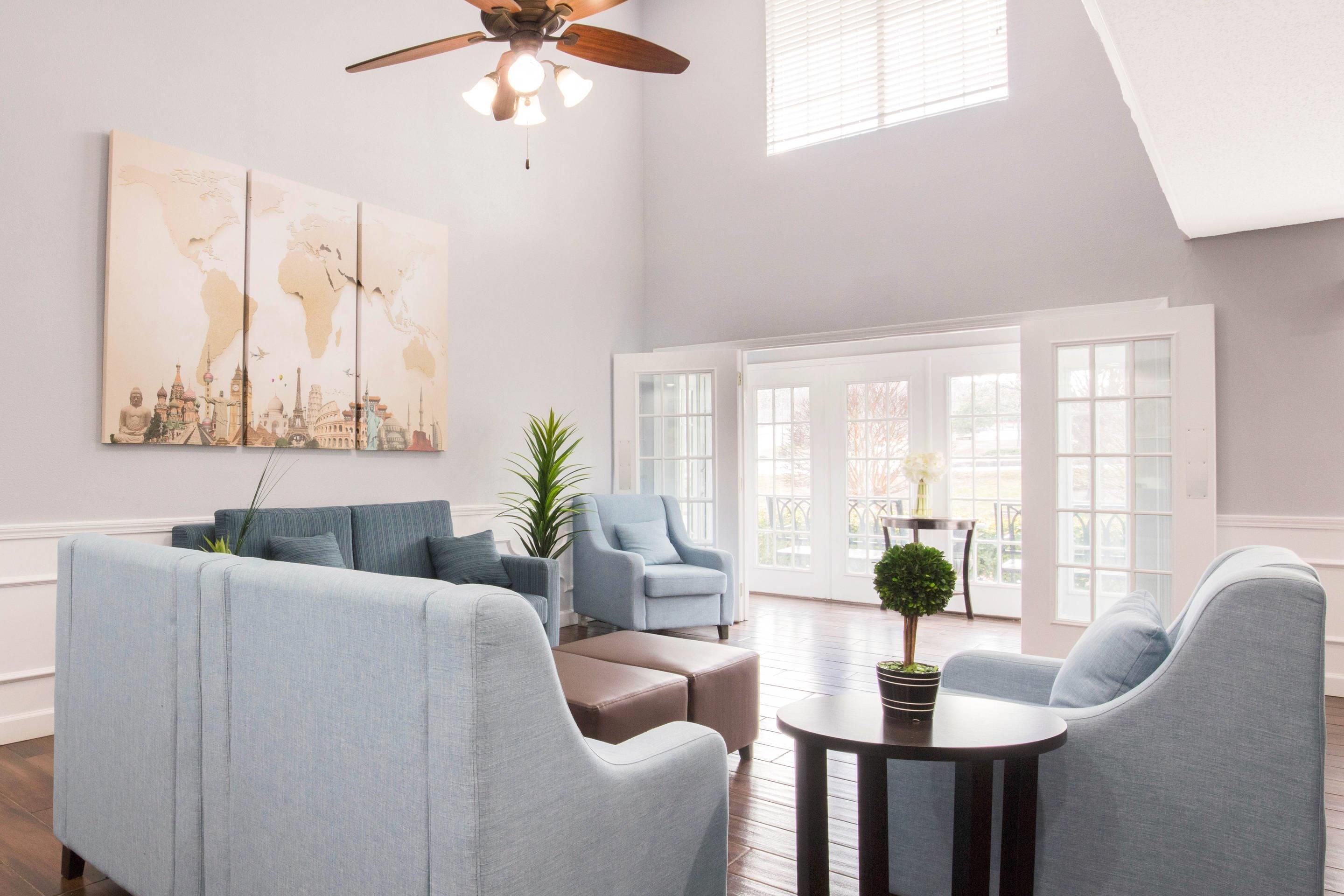 A spacious living room with a high ceiling, a ceiling fan, and large windows.