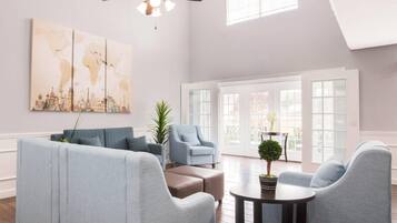 A spacious living room with a high ceiling, a ceiling fan, and large windows.