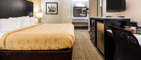 A hotel room with a bed, a desk with a flat-screen TV, a coffee machine, and a mirror.