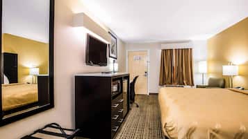 Una habitación de hotel con una cama, un escritorio con televisor de pantalla plana, un espejo, una puerta y una ventana con cortinas.