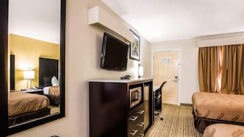 Een hotelkamer met een bed, een bureau, een televisie, een spiegel, een kast en een deur naar een andere kamer.