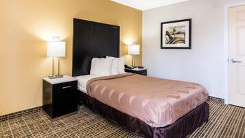 A hotel room with a bed, bedside tables, lamps, a framed picture on the wall, and a door.