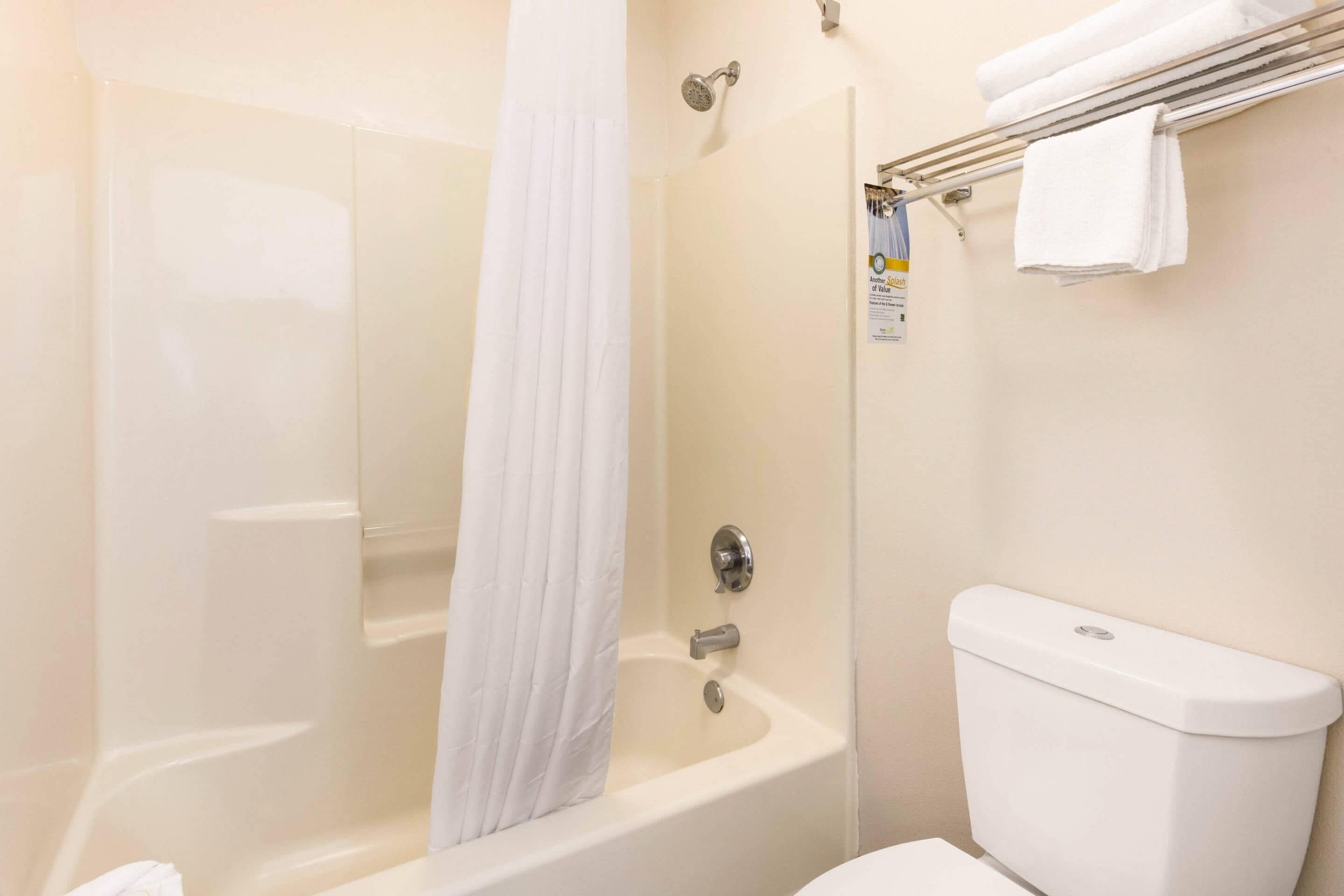 A bathroom with a bathtub, a shower curtain, a toilet, and a towel rack with towels.