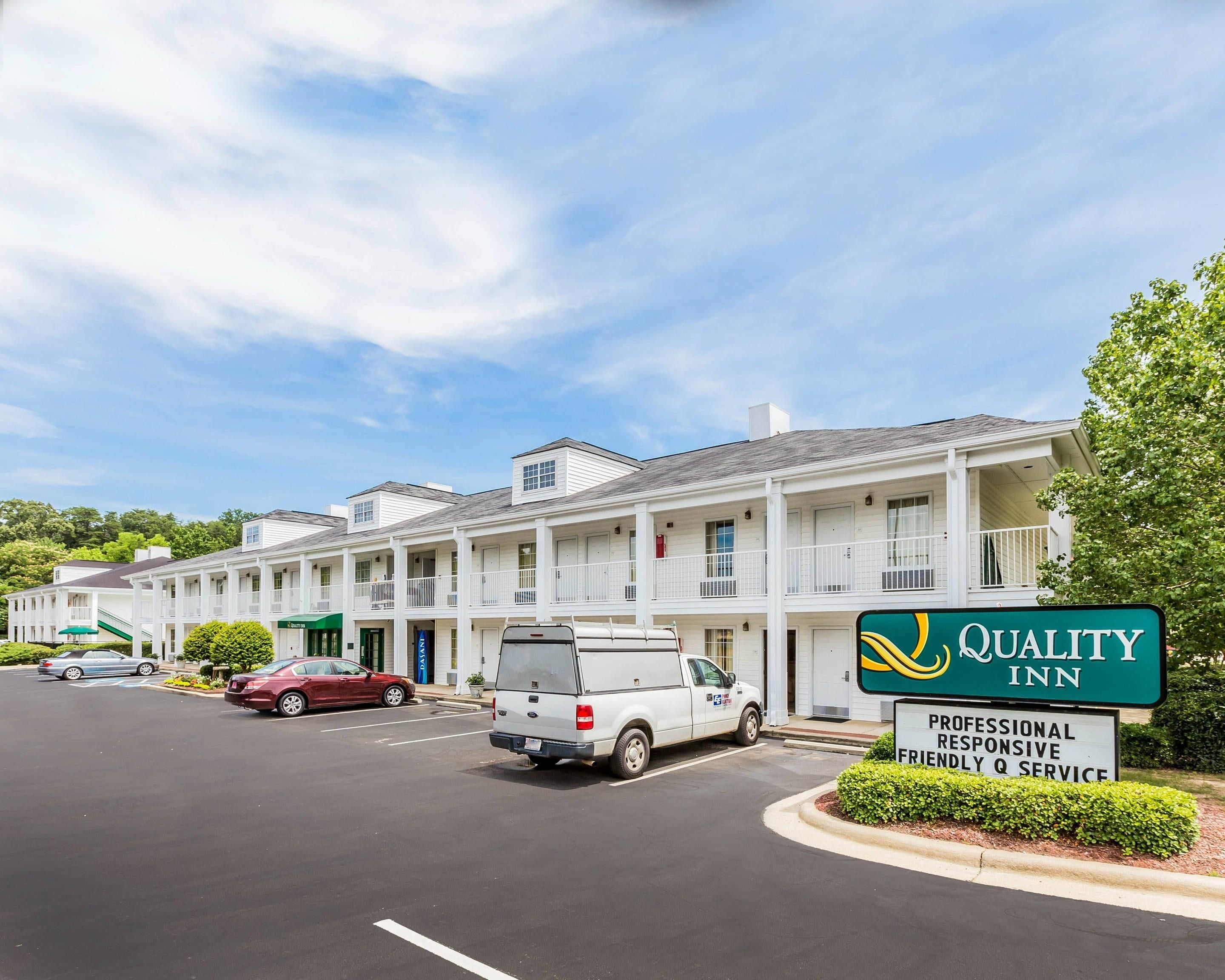 Un motel con un letrero que indica 'Quality Inn' y una descripción que dice 'Servicio Q Profesional, Atento y Amable'.
