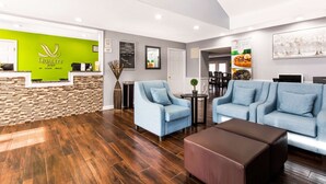 A reception area with a green wall, wooden reception desk, and a seating area with blue sofas and a brown ottoman. - Quality Inn Trussville I-59 exit 141 (Trussville)