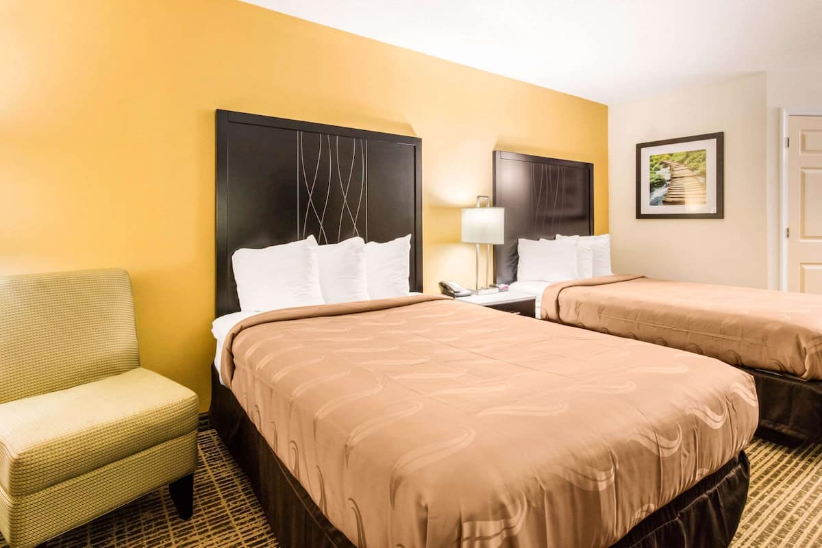 A hotel room with two beds, a chair, a nightstand, and a lamp.