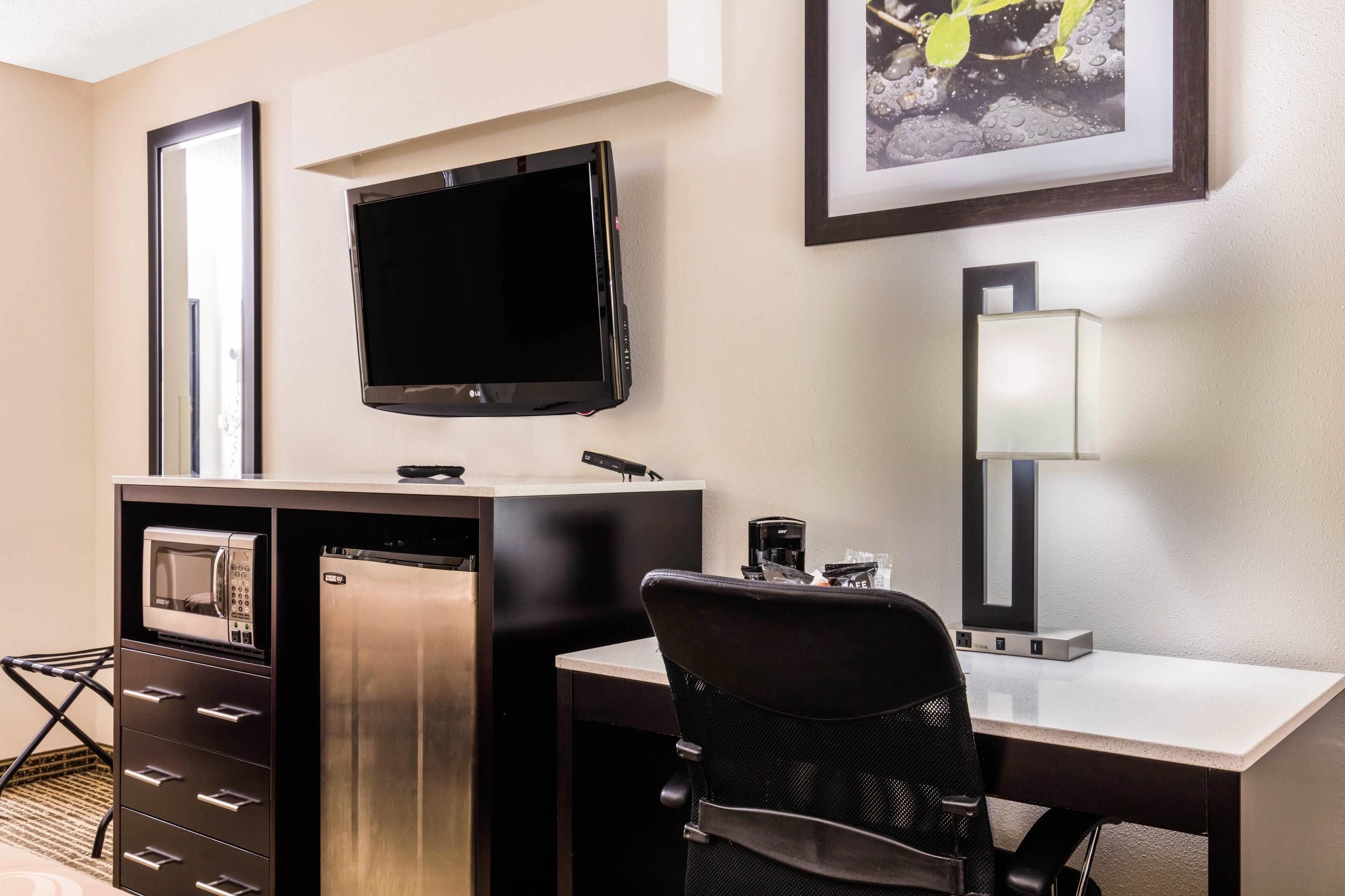 Ein Hotelzimmer mit Schreibtisch, Stuhl, Fernseher, Minibar und einem gerahmten Bild an der Wand.