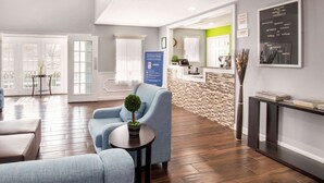 A modern reception area with a reception desk, a seating area with a blue armchair and a small table, and a stone accent wall. - Quality Inn Trussville I-59 exit 141 (Trussville)
