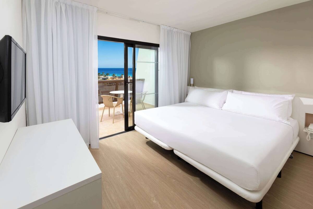 Una habitación de hotel con una cama grande, un escritorio y vistas al océano a través de una puerta corredera.
