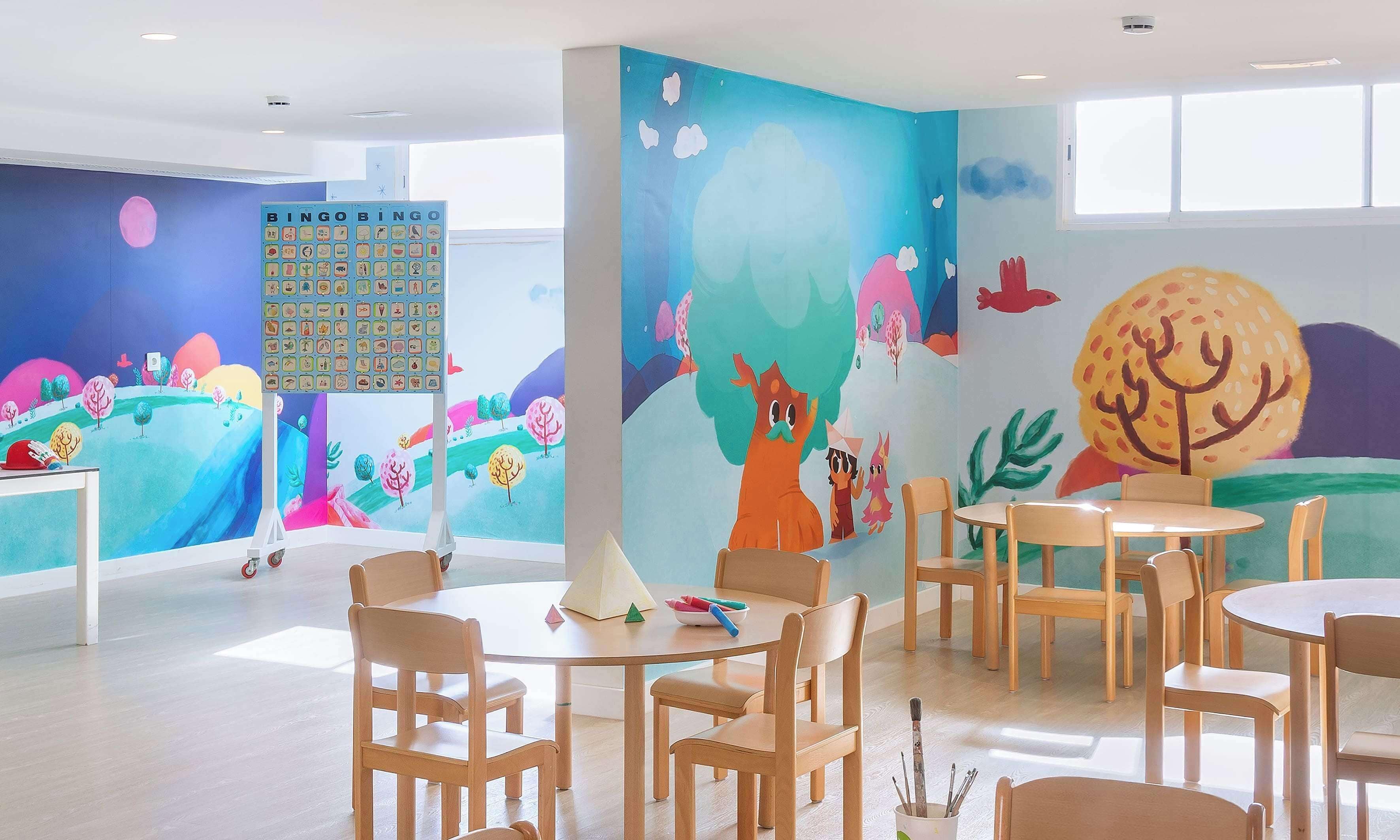 A brightly colored children's playroom with a large BINGO wall, wooden furniture, and a window providing natural light.