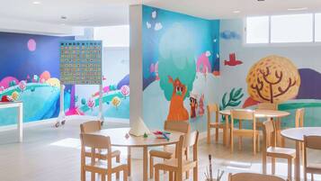 A brightly colored children's playroom with a large BINGO wall, wooden furniture, and a window providing natural light.