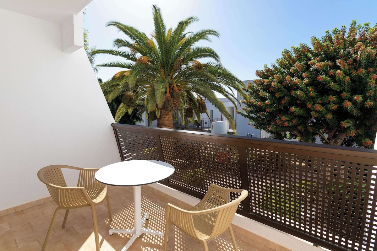A balcony with two wicker chairs and a small round table, surrounded by a wooden lattice fence.