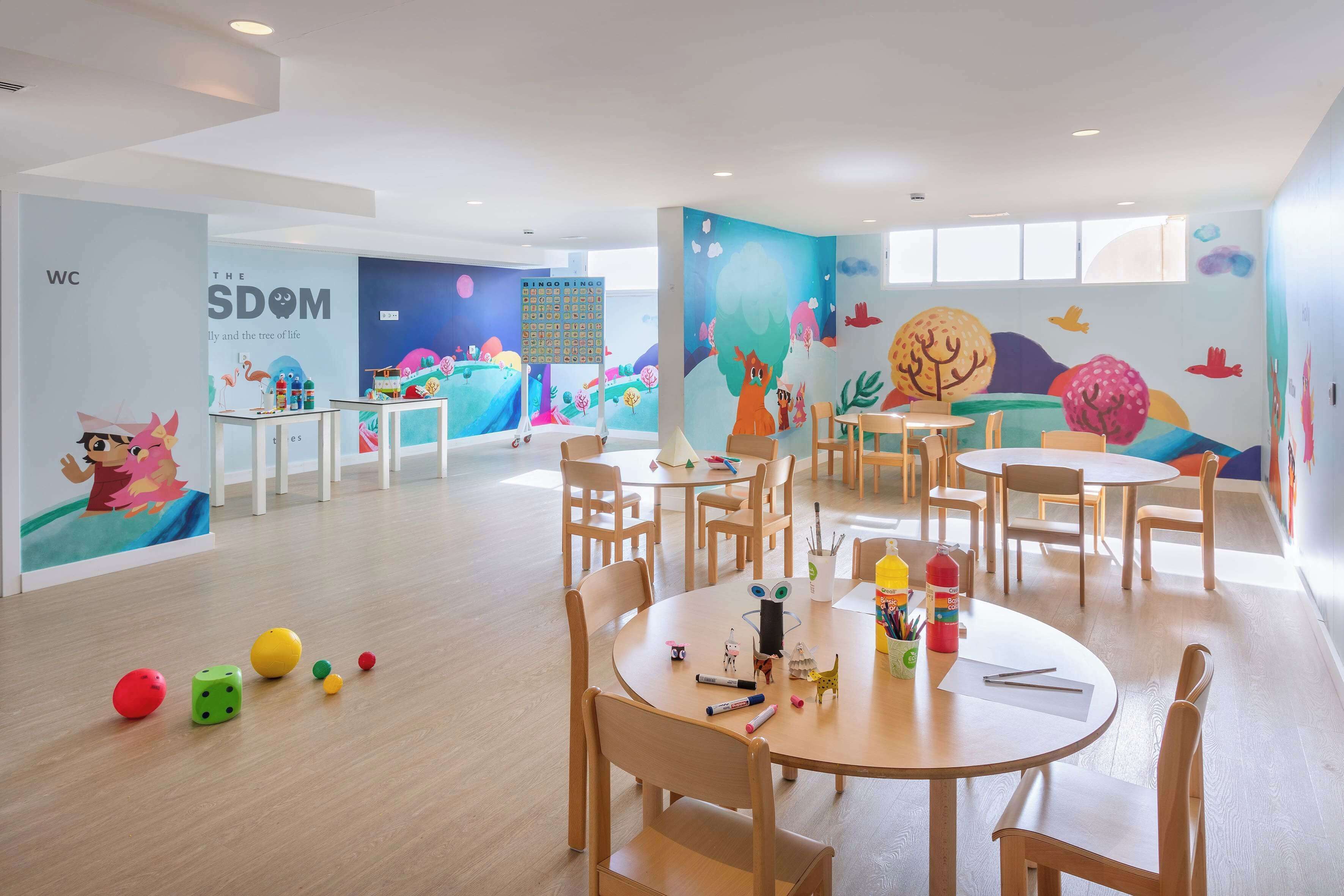A children's playroom with colorful murals, wooden tables, and chairs.