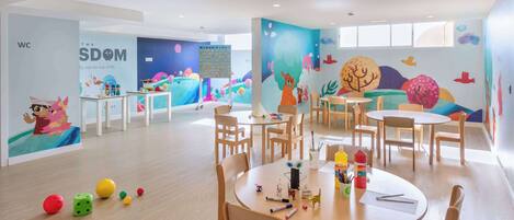 A children's playroom with colorful murals, wooden tables, and chairs.