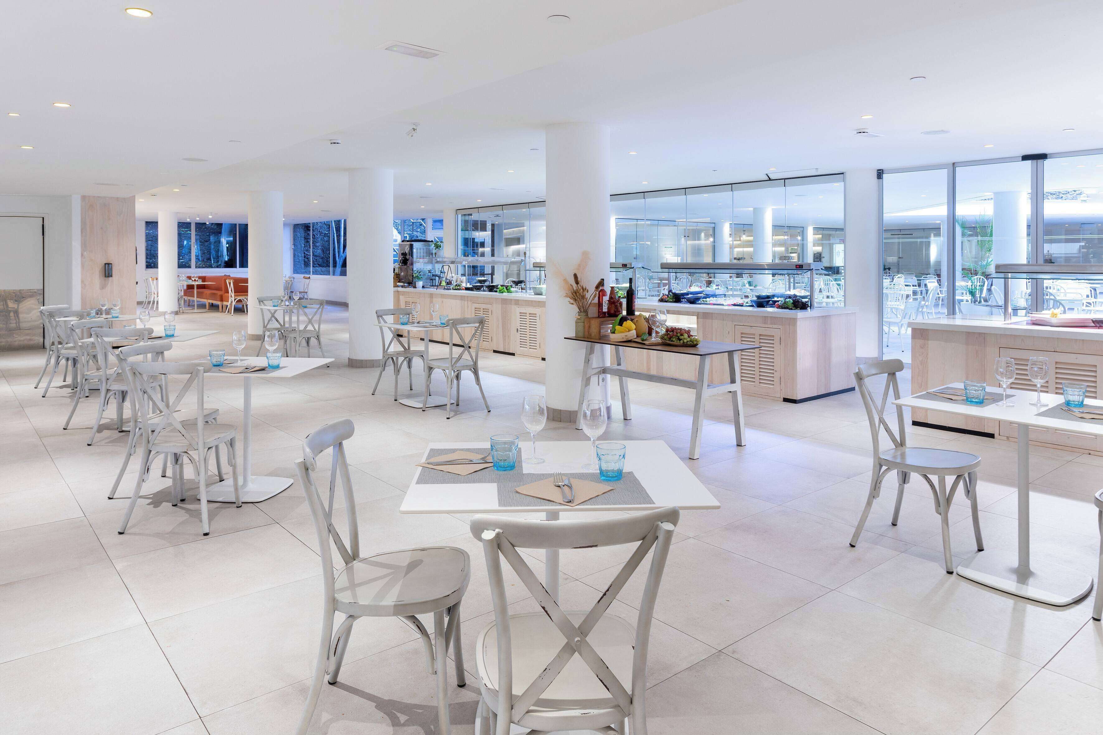A modern restaurant with white furniture, large windows, and a view of the city.