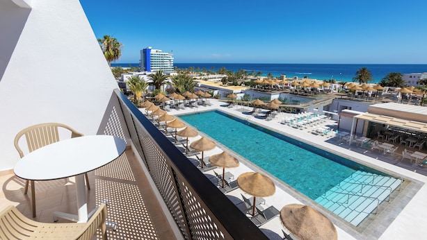 Un espace aménagé au bord de la piscine, avec des chaises longues et des parasols, offrant une vue sur une piscine aux eaux cristallines et sur l’océan.