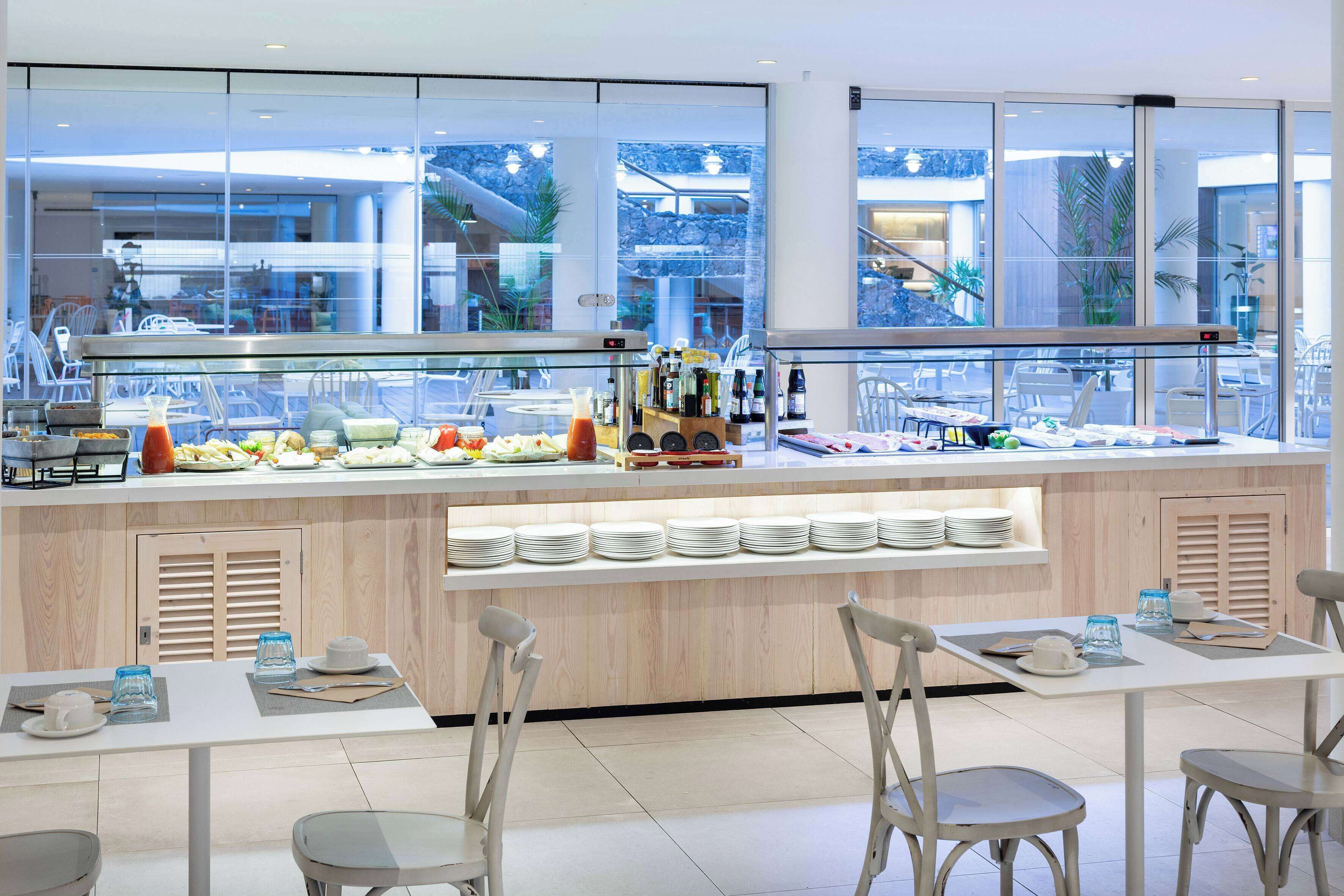 Zona de buffet con una vitrina de vidrio, platos blancos y diferentes opciones de comida.