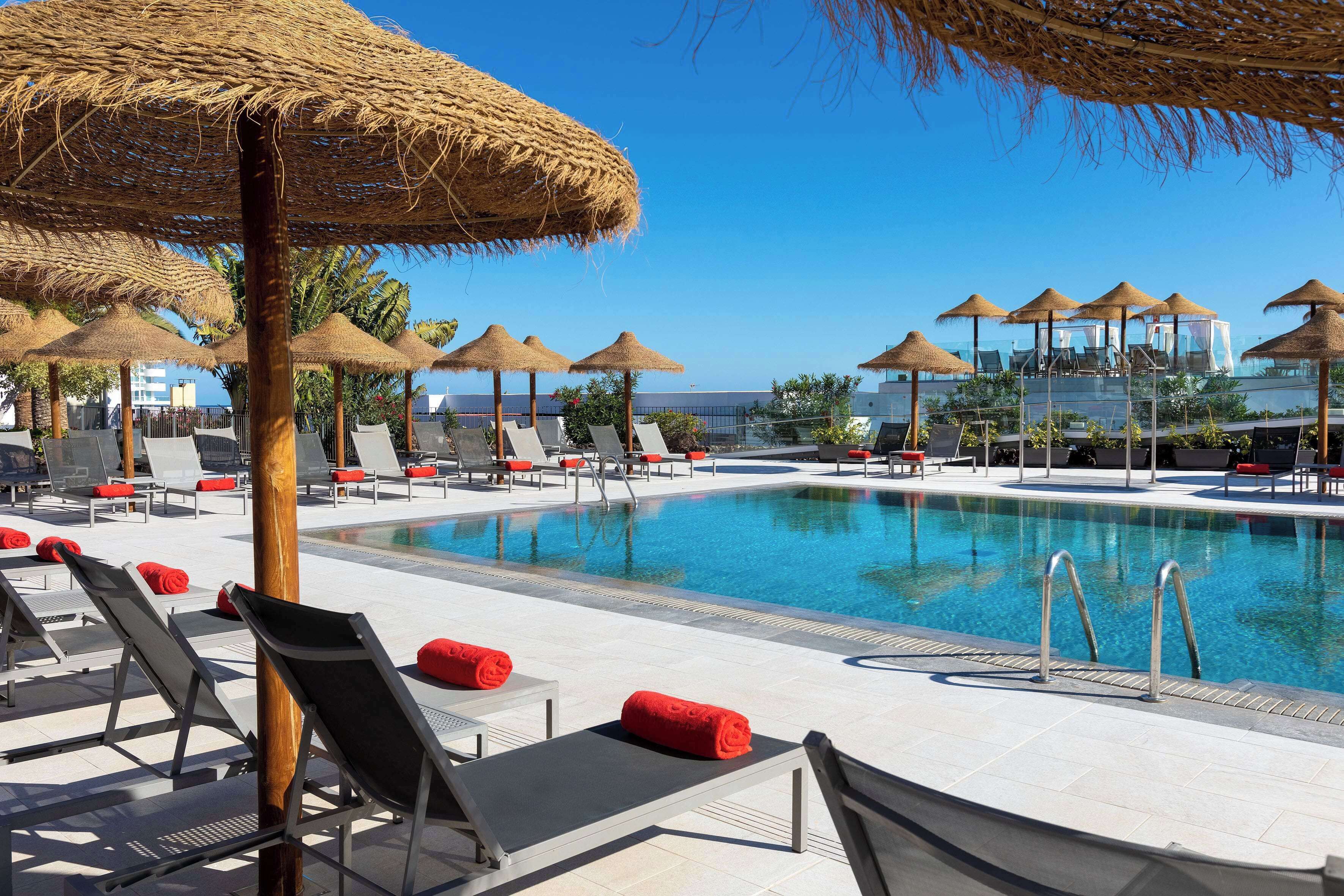A poolside area with lounge chairs and umbrellas, a clear blue pool, and a view of the ocean.