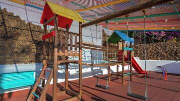 Um parquinho com uma estrutura de escalada de madeira, balanços e um escorrega.