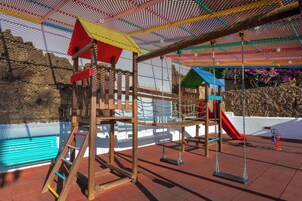 Um parquinho com uma estrutura de escalada de madeira, balanços e um escorrega.