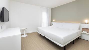 A modern hotel room with a large bed, a small bedside table, a flat-screen TV mounted on the wall, and a bedside lamp.