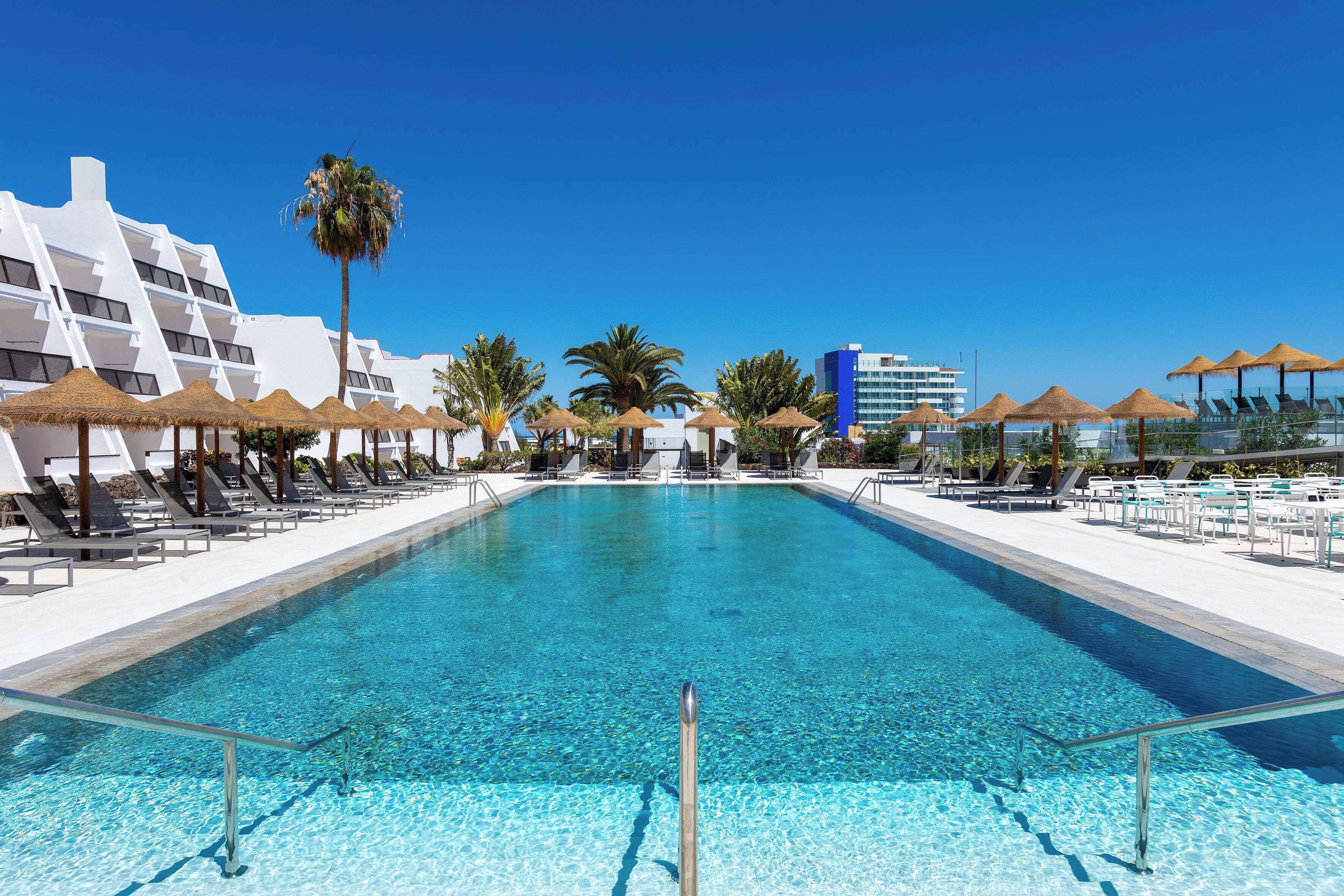 Ein Poolbereich mit klarem, blauem Wasser, Liegestühlen und Sonnenschirmen.