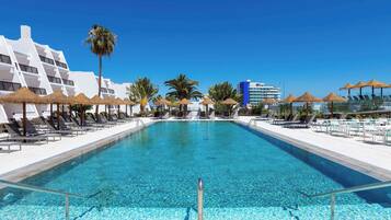 Ein Poolbereich mit klarem, blauem Wasser, Liegestühlen und Sonnenschirmen.