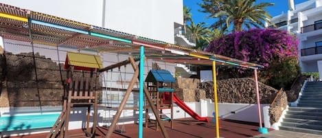 Ein Spielplatz mit Schaukeln, einer Rutsche und einer Kletterkonstruktion.