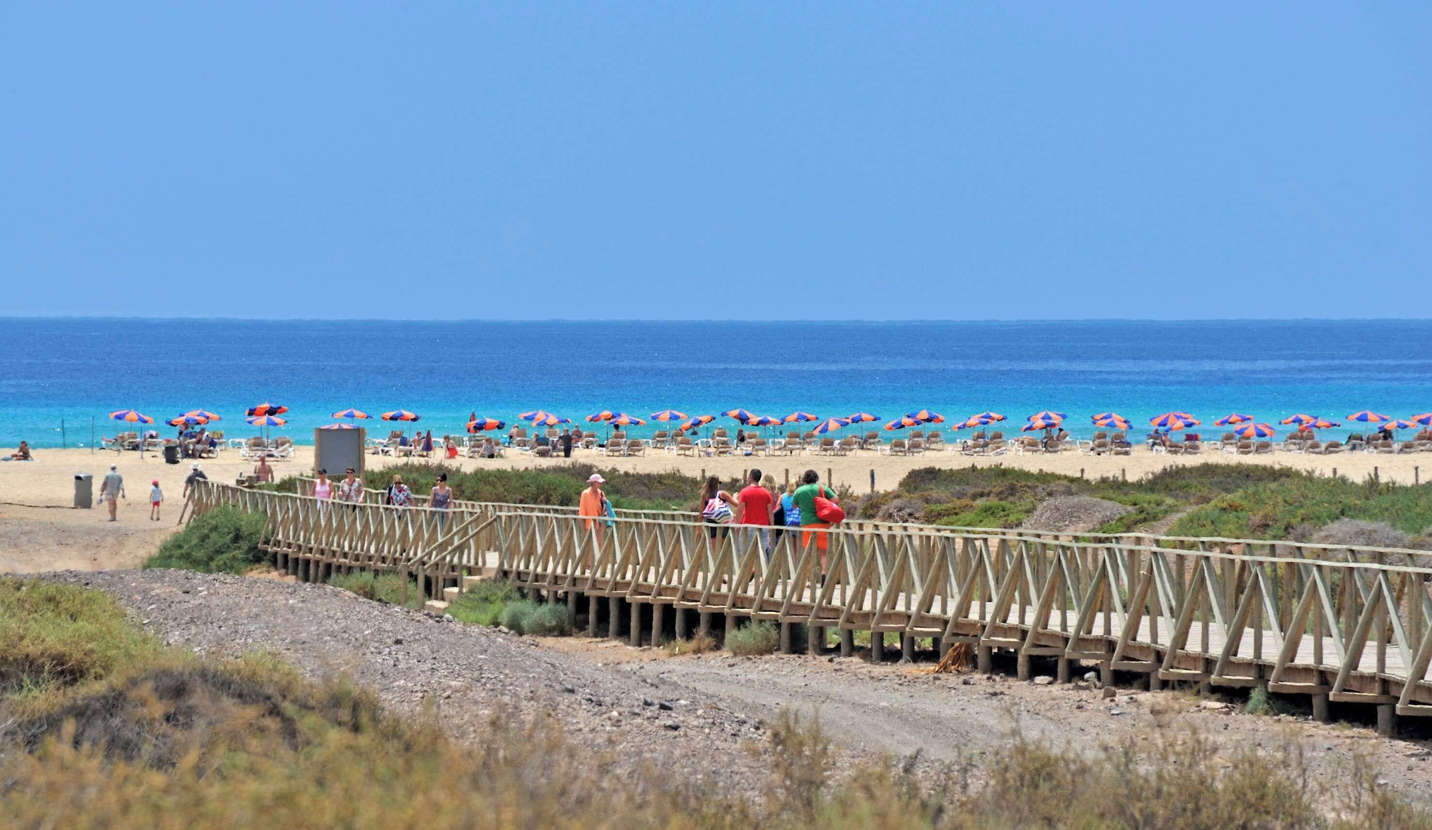 A wooden bridge leading to a beach with umbrellas and people.