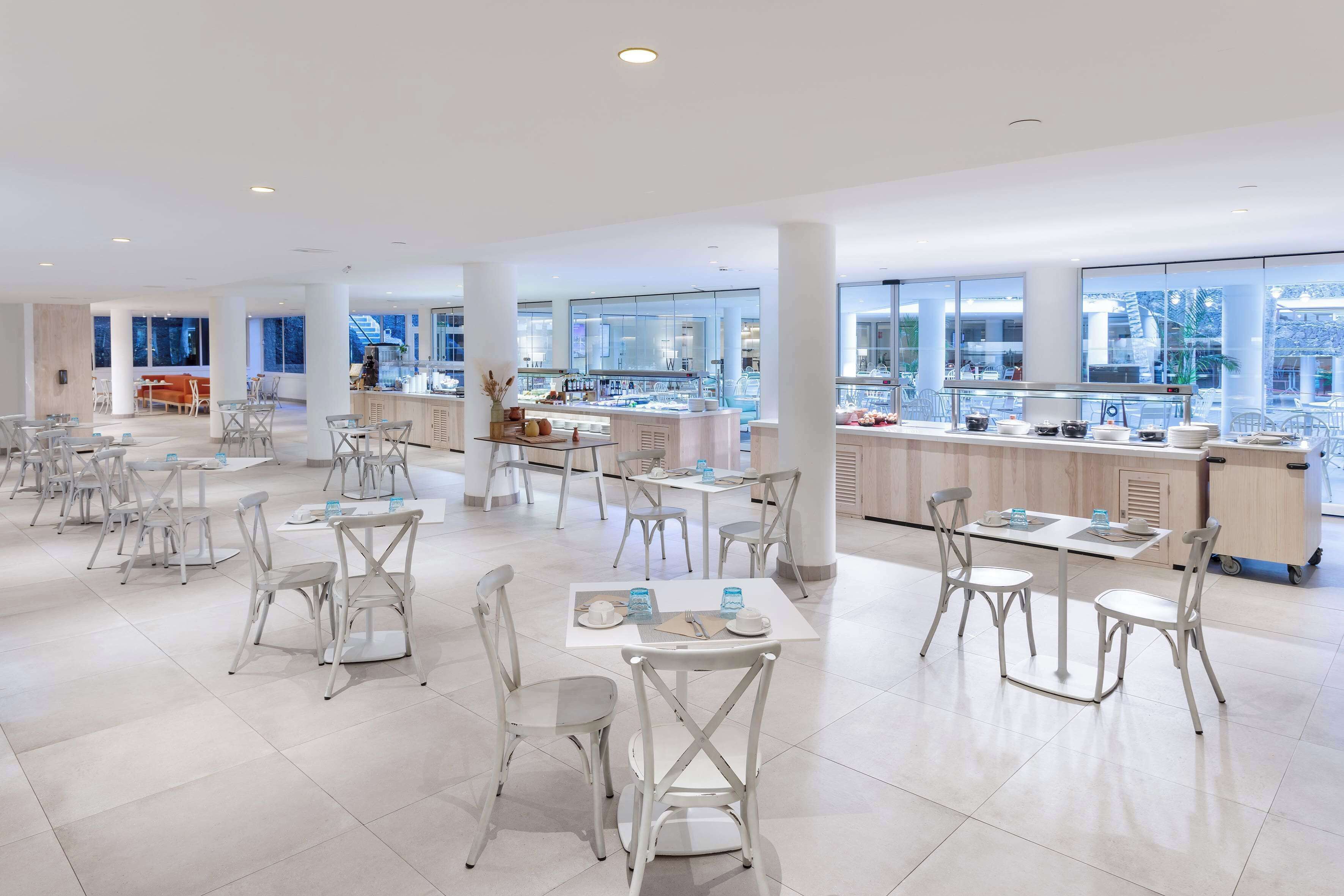 A modern, spacious restaurant with high ceilings, large windows, and a clean, minimalist design.