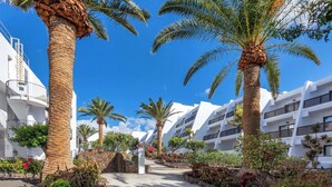 Un sentier bordé de palmiers et un bâtiment blanc doté de balcons.