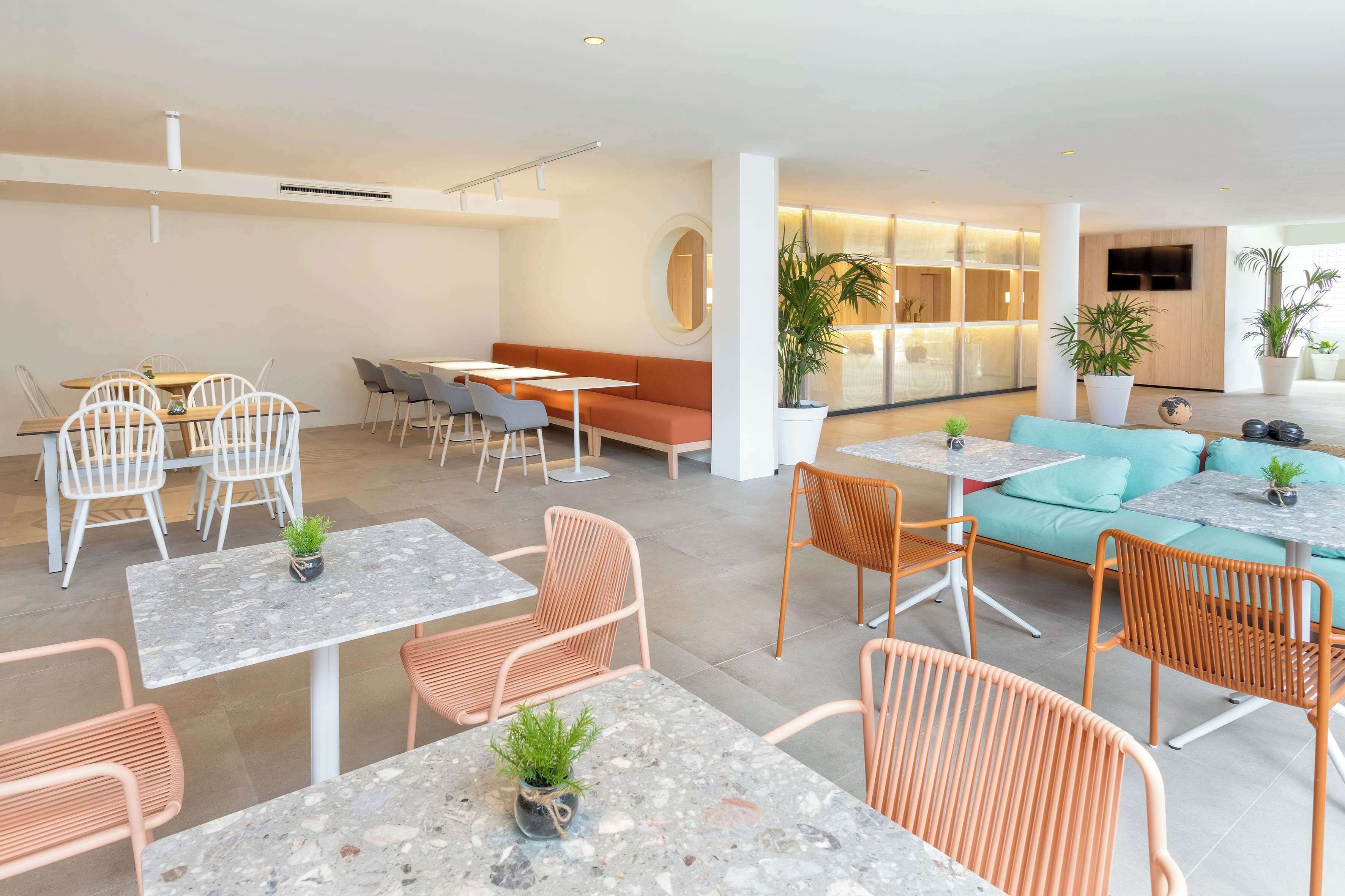 A modern hotel lobby with seating areas, tables, and potted plants.