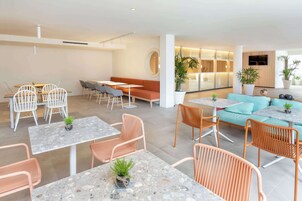 A modern hotel lobby with seating areas, tables, and potted plants.