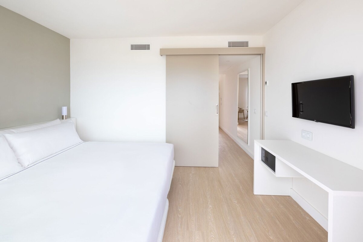 Een moderne hotelkamer met een groot bed, een aan de muur bevestigde televisie en een inloopkast.