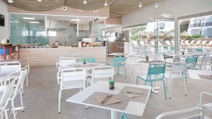 Un restaurant moderne avec des chaises blanches et turquoise, un bar central et de grandes fenêtres donnant sur un espace piscine.