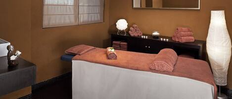 A spa room with a massage table, towels, a mirror, and a vase of flowers.